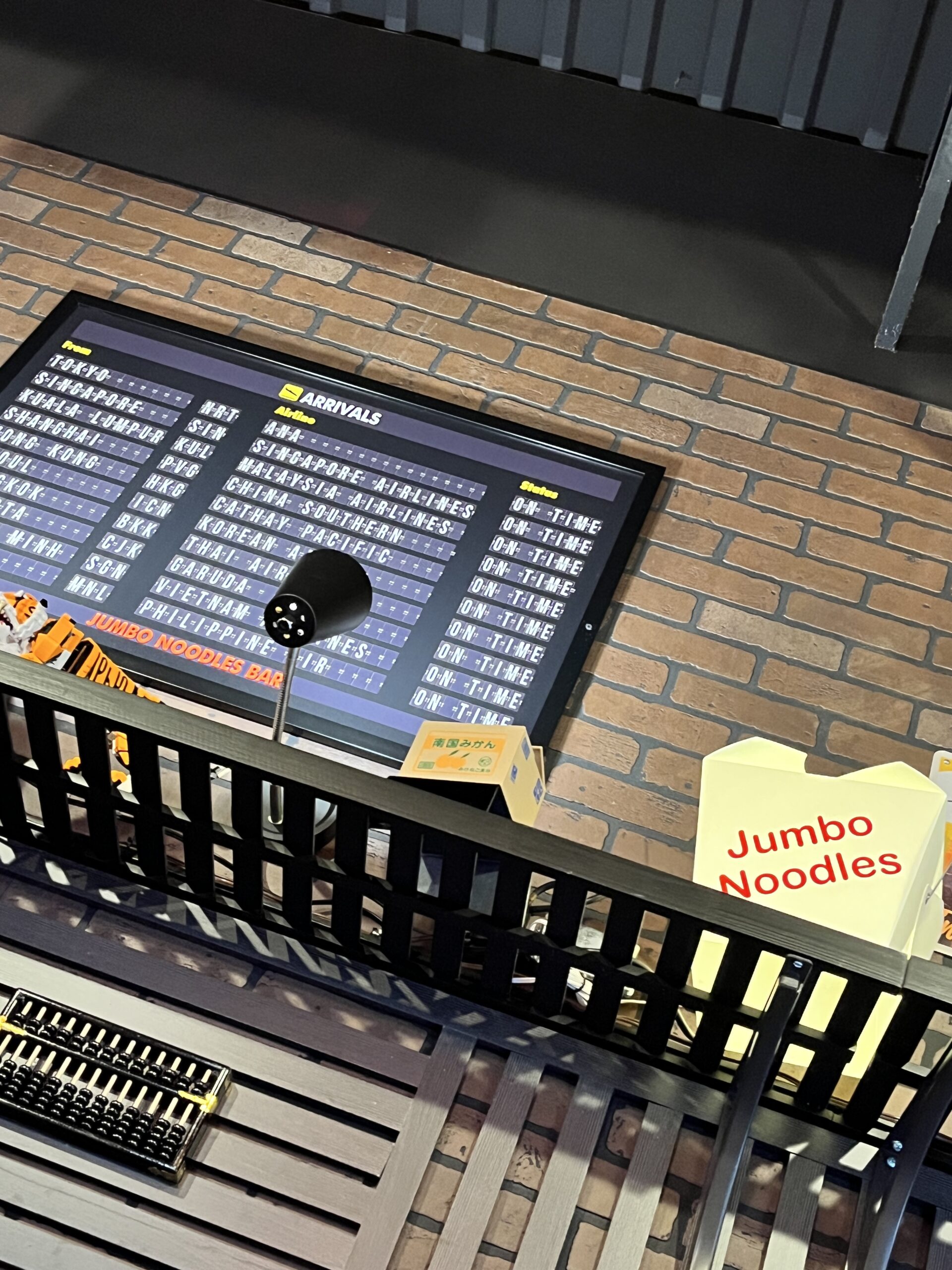Decorative airport-themed wall featuring an arrivals board and oversized food props, including a takeout container labeled "Jumbo Noodles."